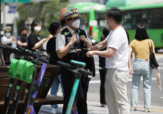 A police officer stops an electric scooter driver in Hongdae, western Seoul, on Thursday. According to an amendment to the Road Traffic Act, unlicensed e-scooter riders are subject to a 100,000 won fine from Thursday. Those caught riding without helmets face a 20,000 won fine. A 40,000-won fine is imposed if two or more people are seen riding an e-scooter. [YONHAP]