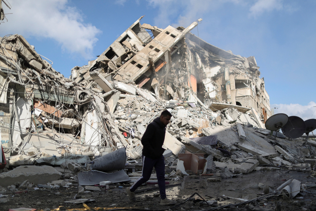 이스라엘군의 공습으로 파괴된 팔레스타인 가자지구의 건물 폐허 사이를 13일(현지시간) 한 주민이 지나고 있다./로이터연합뉴스