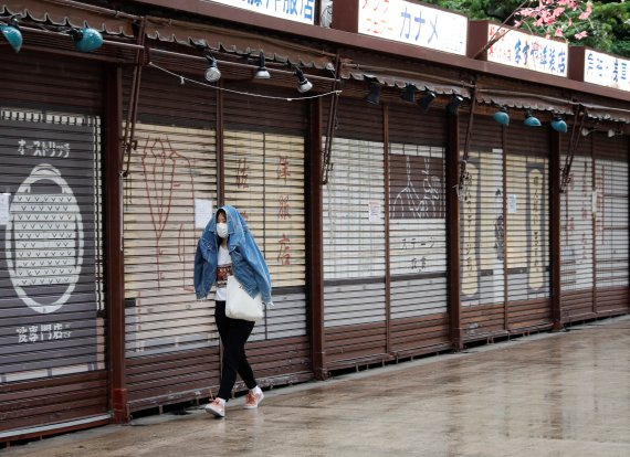 지난 7일 한 여성이 외투로 비를 가리며, 도쿄의 유명 관광지인 아사쿠사 상점가를 거닐고 있다. 코로나19 확산 방지를 위한 긴급사태 선언 여파로 점포들이 문을 닫고 있다. 로이터 뉴스1