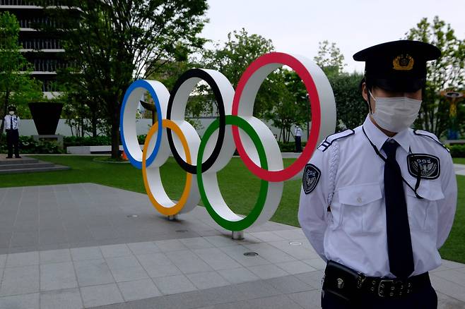 지난달 18일 도쿄올림픽 개최 반대 시위가 벌어진 도쿄의 일본올림픽조직위원회 본부 앞 올림픽 조형물 앞에서 경비원이 경계를 서고 있는 모습.