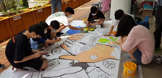 행사장에 참여한 청소년들이 바닥에 펼쳐진 밑그림에 색과 글씨를 채워 넣어 ‘민주화’를 완성하고 있다.[사진=광주시교육청]