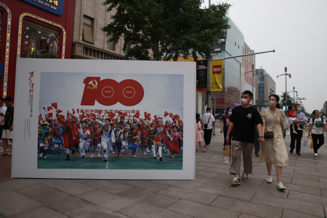 중국에서 단오절 연휴인 지난 13일 베이징의 주요 쇼핑가 왕푸징 거리에서 ‘공산당 100주년’ 홍보판 옆으로 관광객들이 지나가고 있다. /EPA연합뉴스