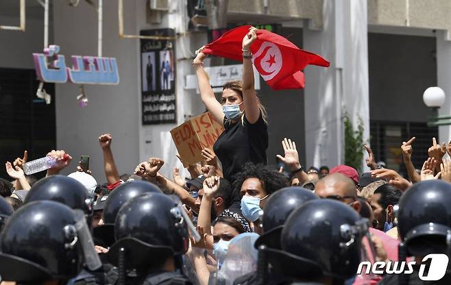 25일(현지시간) 튀니지 수도 튀니스의 국회의사당 앞에서 반정부 시위가 열렸다. 한 여성이 시위대를 가로 막은 경찰 앞에서 국기를 흔들고 있다. © AFP=뉴스1 © News1 이정후 기자