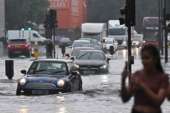 25일(현지시간) 영국 런던 나인 엘름스 지역에서 차량들이 많은 비로 물에 잠긴 도로를 헤쳐나가고 있다. 이날 런던 곳곳에서는 천둥을 동반한 폭우가 내리면서 도로가 침수되고 많은 버스와 승용차들의 발이 묶이는 사태가 벌어졌다.