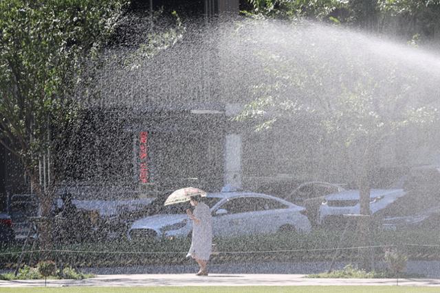 연일 폭염이 이어지고 있는 26일 오전 잔디밭에 물을 주고 있는 서울광장 옆으로 한 시민이 양산을 쓰고 걸어가고 있다. 연합뉴스