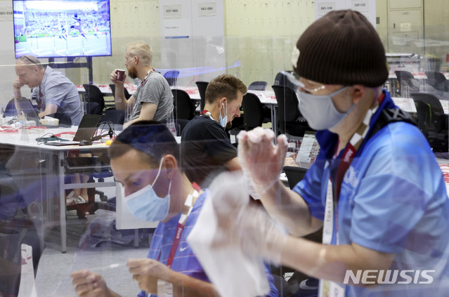 [도쿄(일본)=뉴시스] 최진석 기자 = 2020 도쿄올림픽 개막을 하루 앞둔 22일 일본 도쿄 올림픽 메인프레스센터(MPC)에서 가림막 소독 작업을 하는 자원봉사자 뒤로 한 외신기자가 마스크를 내린 채 업무를 보고 있다. 2021.07.22. myjs@newsis.com