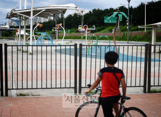 자전거를 타고 지나가던 한 어린이가 운영중단된 물놀이장을 바라보고 있다.