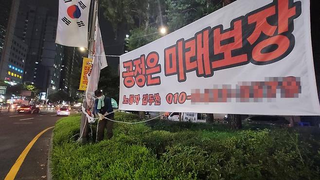 지난 14일 오후 김두찬씨가 서울 강남역사거리에 설치한 현수막을 정리하고 있다 [촬영 조다운]