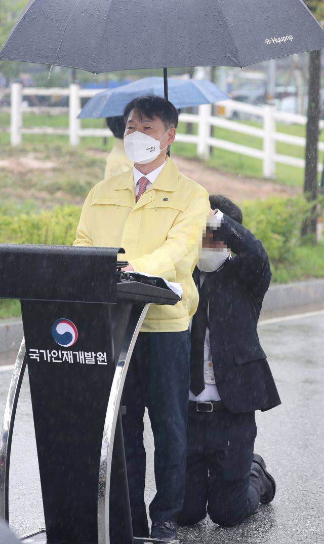 강성국 법무부 차관이 27일 오전 충북 진천 국가공무원인재개발원에서 아프가니스탄 특별입국자 초기 정착 지원과 관련해 브리핑하는 도중 관계자가 뒤쪽에서 무릎을 꿇고 우산을 받쳐주고 있다. 연합뉴스