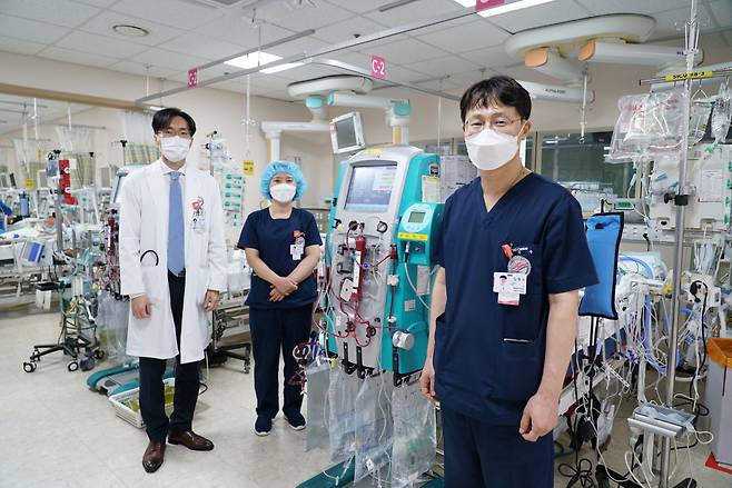 In this photo taken Sept. 2, Hallym University Sacred Heart Hospital's ECMO team stands before a former COVID-19 patient undergoing mechanical support and recovering. From left, respiratory disease specialist Dr. Park Sung-hoon; ECMO coordinator and head nurse Lee Sun-hee; chest surgeon Dr. Kim Hyoung-soo. (Kim Arin/The Korea Herald)