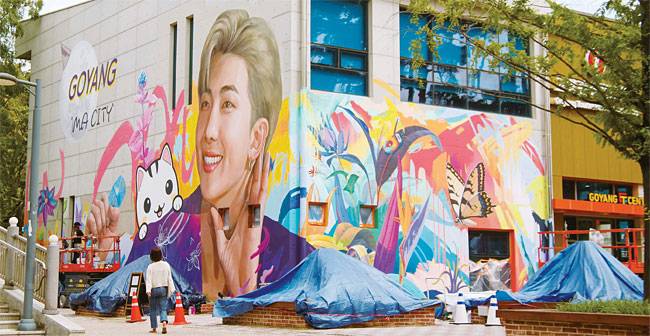 방탄소년단(BTS)의 리더 RM의 고향인 경기 고양시에 그의 얼굴로 건물 벽면을 가득 채운 벽화가 등장했다. 고양시는 BTS 팬클럽 아미와 협력해 일산동구 고양관광정보센터 건물 벽면에 가로 18m, 세로 12m 규모의 대형 벽화를 조성했다. 벽화는 RM의 생일인 10월 12일에 맞춰 완성될 예정이다. 사진 연합뉴스