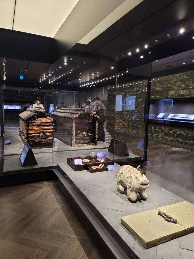 무령왕릉의 내부를 재현한 국립공주박물관의 백제웅진실 전경. 무령왕에 대해 적은 묘지명과 진묘수 뒤로 왕과 왕비를 위한 제사상이 차려져 있고 그 뒤에 목관이 나란히 놓인 발견 상태 그대로 전시 중이다.