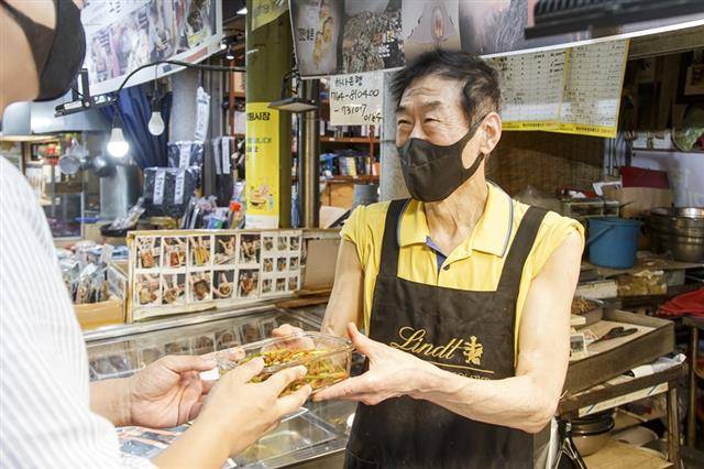 ‘친환경 전통시장’을 선언한 서울 마포구 망원시장의 한 상인(오른쪽)이 고객에게 일회용품이 아닌 다회용기에 담긴 반찬을 건네고 있다.마포구 제공