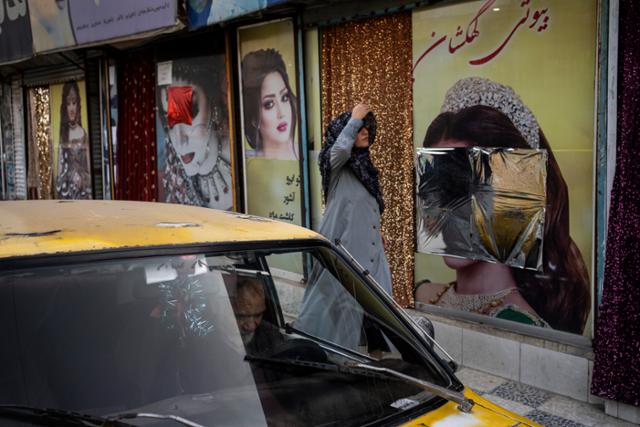 아프가니스탄 수도 카불에서 12일 외벽 광고 속 여성들의 얼굴이 가려진 미용실 앞을 한 여성이 걸어가고 있다. 카불=AP 연합뉴스