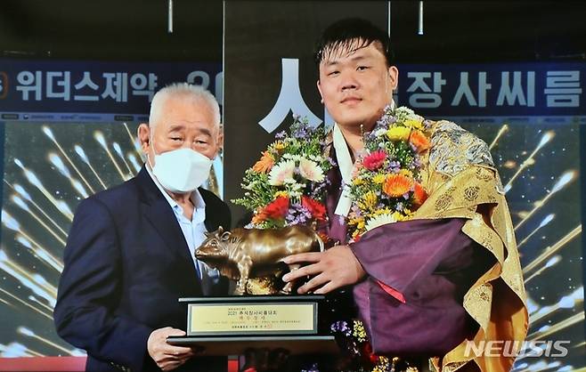 [증평=뉴시스] 강신욱 기자 = 충북 증평군청 인삼씨름단 소속 천하장사 김진이 21일 충남 태안종합체육관에서 열린 위더스제약 2021 추석장사씨름대회에서 백두장사에 등극한 뒤 황경수 대한씨름협회장으로부터 황소 트로피를 받고 있다. (사진=KBS TV 촬영) 2021.09.21. ksw64@newsis.com