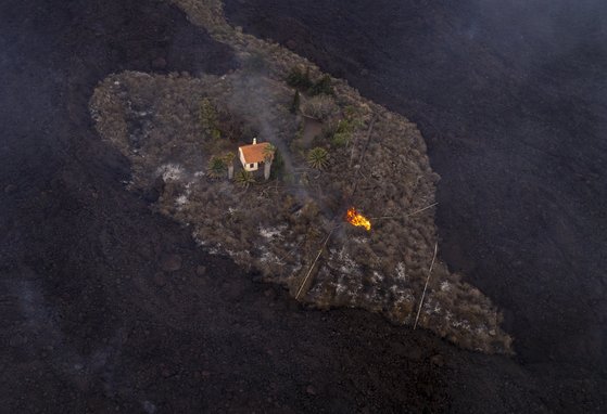지난 19일(현지시간) 시작된 스페인 카나리아제도 라팔마 섬 쿰브레 비에하 국립공원 내 화산폭발에서 주황색 지붕의 주택 한채가 기적적으로 피해를 입지 않았다. 사진의 검은색 땅은 모두 용암과 화산재로 뒤덮인 것이다. AP=연합뉴스