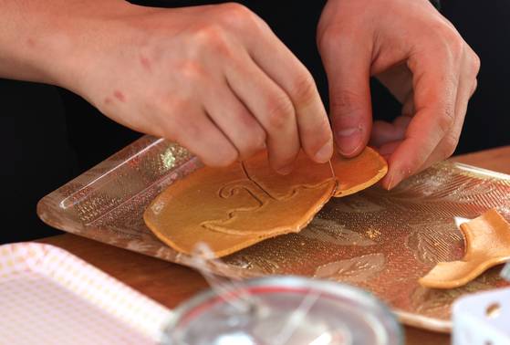 서울 종로구 대학로의 한 뽑기 가게에서 한 시민이 우산 모양 뽑기를 하고 있다. 이 가게 주인 안영희씨는 넷플릭스 '오징어 게임'에 등장한 달고나 뽑기 700여개를 직접 제작했다. 연합뉴스