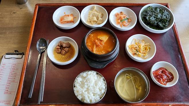 The Cheongdamgol (From top-left to bottom-right) baechu kimchi(cabbage kimchi), eomuk bokkeum(stir-fried fish cake), geonsaeu bokkeum(stir-fried dried shrimp), gim gui(roasted seaweed), dwaejigogi jangjolim(soy sauce braised pork), dubu gimchijjigae (kimchi stew with tofu), kongnamul muchim (seasoned soybean sprouts), ojingeojeot (salted squid), kongnamulguk (soybean sprout soup) (Kim Hae-yeon/ The Korea Herald)