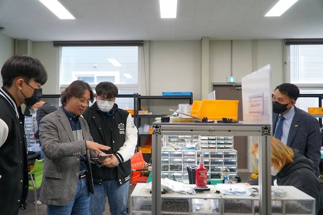 20일 오전, 충남 아산시 아산테크노밸리에 위치한 ㈜미래기계기술에서 신승무(왼쪽) 대표이사가 사내 연구소 시제품 조립실에서 임상호(오른쪽) 지도교수가 지켜보는 가운데 현장수업에 참석한 대학생들에게 카메라 모듈 테스트 소켓을 설명하고 있다. 사진=스마트4차산업혁명협회.