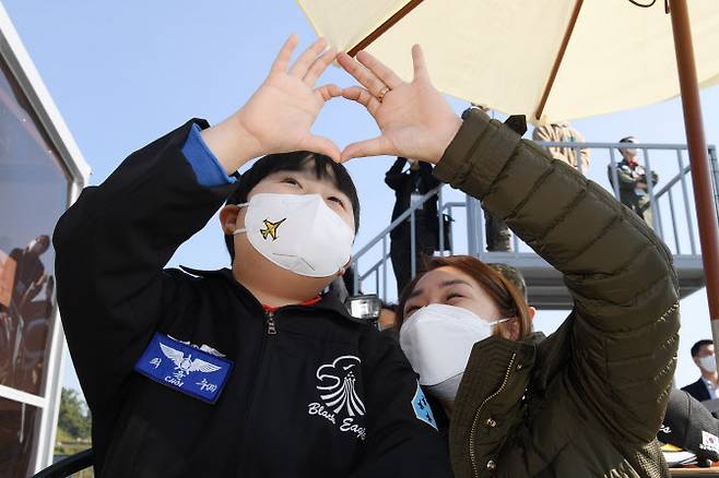 공군 특수비행팀 블랙이글스가 22일 ‘서울ADEX 2021’이 진행 중인 경기도 성남 서울공항에서 희귀 소아암으로 투병 중인 최윤수 군을 위한 특별 이벤트를 마련했다. 사진은 블랙이글스가 에어쇼에서 하트를 그리자 어머니와 손 하트를 만들어 보이는 최윤수 군(왼쪽)의 모습(사진=공군 제공).