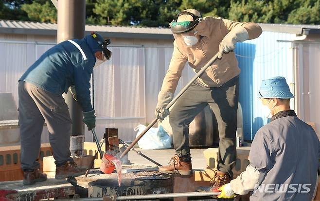 [진천=뉴시스] 강신욱 기자 = 국가무형문화재 112호 원광식 주철장이 22일 충북 진천군 덕산읍 성종사에서 전통밀랍주조기법으로 범종 제작과정을 공개시연한 가운데 작업자들이 도가니에 쇳물을 옮겨 붓고 있다. 2021.10.22. ksw64@newsis.com