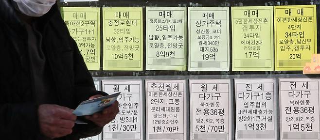 서울 서대문구의 부동산 중개업소에 게시된 매물 가격 안내판 앞을 한 시민이 은행 통장을 든 채 지나가고 있다. /연합뉴스