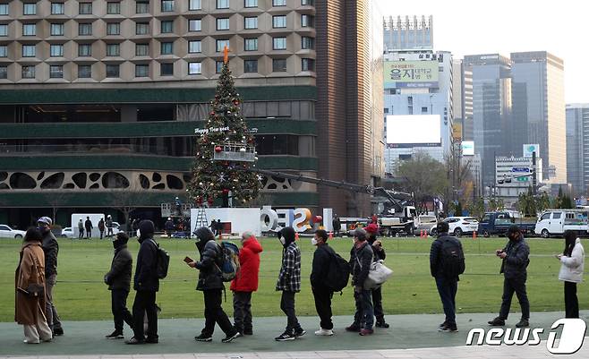 지난 24일 서울광장에 크리스마스 트리가 설치되고 있다. 설치되는 크리스마스 트리 뒤로 선별진료소 검사를 받기 위해 길게 줄을 선 시민들이 보인다. /뉴스1 © News1 신웅수 기자