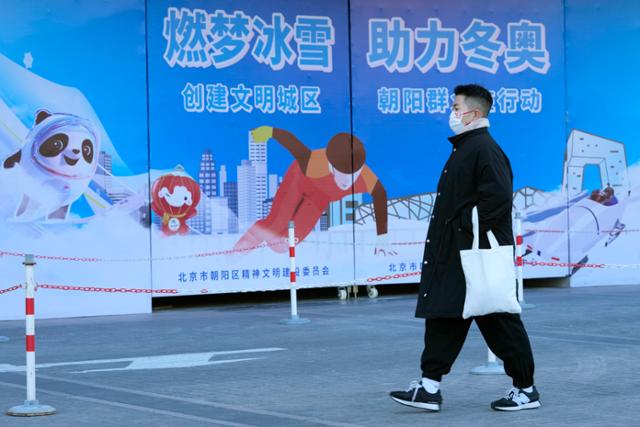 중국 베이징의 한 거리에 설치된 올림픽 광고판 앞으로 22일 마스크를 쓴 남성이 걸어가고 있다. 베이징=AP 연합뉴스