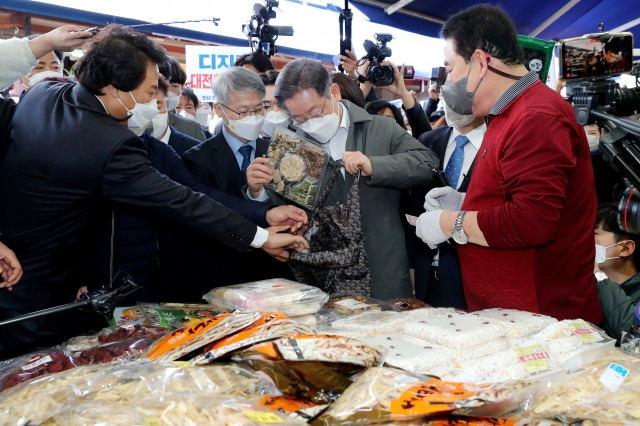 더불어민주당 이재명 대선 후보가 28일 광주시 광산구 송정시장을 방문해 건어물 상점을 찾아 오곡강정을 구입하고 있다. 연합뉴스.