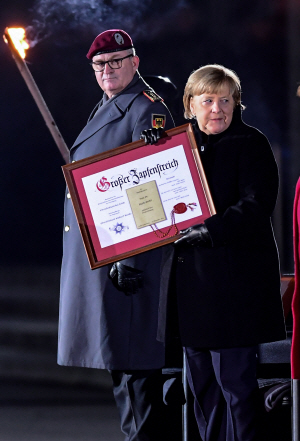 앙겔라 메르켈(오른쪽) 독일 총리가 2일 베를린 국방부 청사 앞에서 열린 퇴임식에서 군악대 환송을 받은 뒤 독일 연방군이 수여한 ‘최고 명예시민상’을 들어 보이고 있다. EPA 연합뉴스
