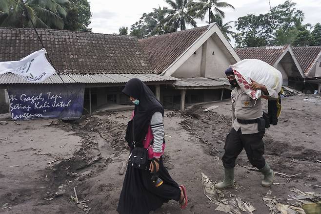 인도네시아 자바섬의 경찰(오른쪽)이 화산 폭발로 집을 잃은 주민을 도와 짐을 옮기고 있다. 뒤로 보이는 집들이 화산재에 반쯤 묻혀 있다. EPA=연합뉴스