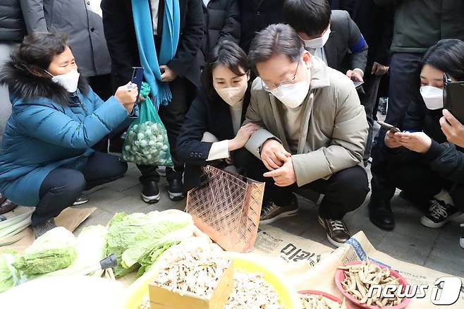 이재명 더불어민주당 대선 후보와 부인 김혜경 씨가 12일 오전 경북 예천군 예천읍 상설시장을 찾아 나물을 구입하기 위해 살펴보자 한 시민이 이 모습을 휴대전화 카메라로 찍고 있다. 2021.12.12/뉴스1 © News1 공정식 기자