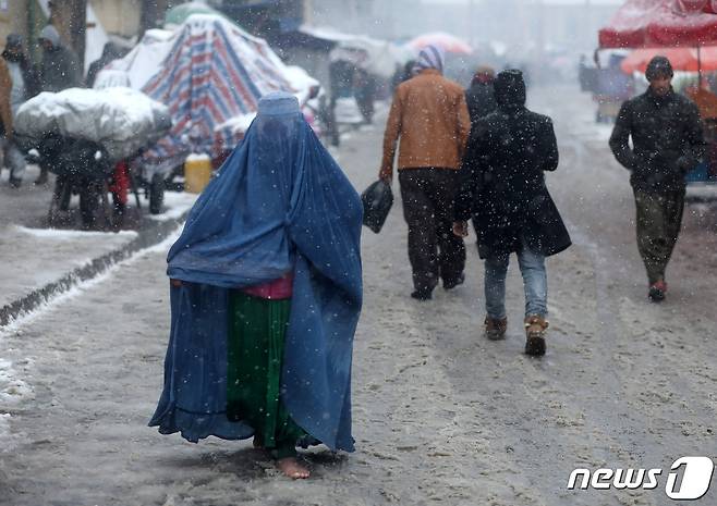 눈이 잘 내리지 않는 아프가니스탄 카불에서 2022년 1월 3일 거리가 하얀 눈으로 덮인 모습. 부르카를 쓰고 힘겹게 걸어가는 여성의 모습도 보인다. © 로이터=뉴스1 © News1 최서윤 기자