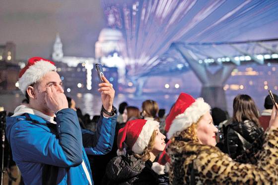 산타클로스 모자를 쓴 사람들이 지난 1일 런던 밀레니엄브리지에서 새해맞이 빛축제를 즐기고 있다. [AP=연합뉴스]