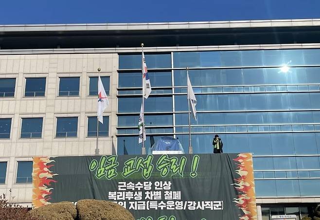 경기교육공무직본부의 고공농성 모습.  임병순 경기교육공무직본부 지부장은 17일 경기도교육청 남부청사 건물 현관 캐노피 위에 올라 고공 농성을 시작했다. 경기교육공무직본부는 유치원 방과후전담사의 기본급 지급 기준을 타 시·도교육청과 동일한 '1유형'으로 전환하라고 촉구해왔다. [촬영 이영주]