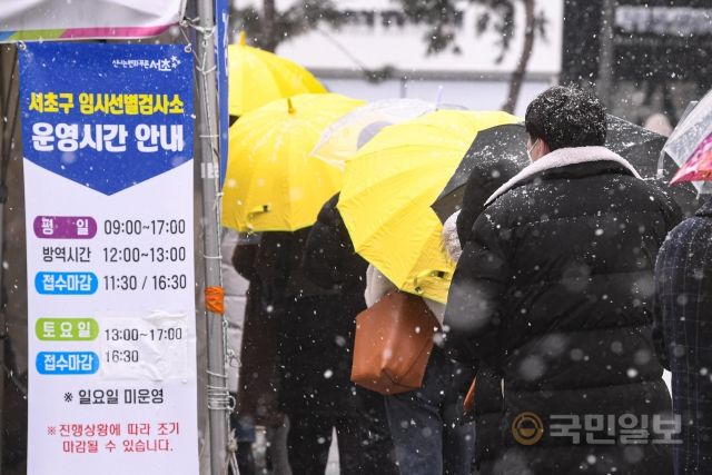눈이 내리는 19일 서울 서초구 강남역 임시선별검사소에서 검사를 받기 위해 방문한 시민들이 우산을 쓴 채 줄지어 서 있다.