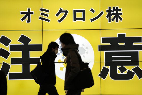 24일 일본 도쿄에서 마스크를 쓴 시민들이 오미크론 변이 주의를 경고하는 전광판 앞을 지나고 있다. [AP=연합뉴스] \