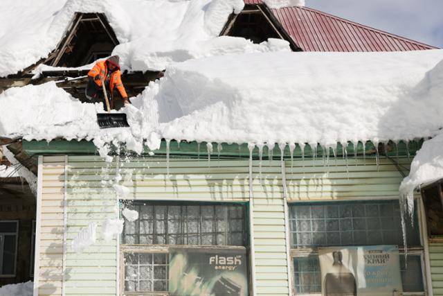 눈폭풍이 강타한 25일 러시아 크라스노다르 준주 고르니 마을에서 한 주민이 지붕 위에 산더미처럼 쌓인 눈을 치우고 있다. 고르니=타스 연합뉴스