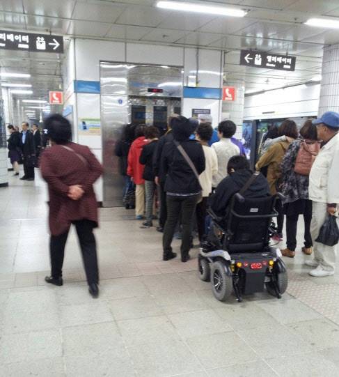 한 지하철역 엘리베이터에서 전동휠체어를 탄 장애인이 일반 이용객들 뒤편으로 밀려나 있다. 누리꾼 제공