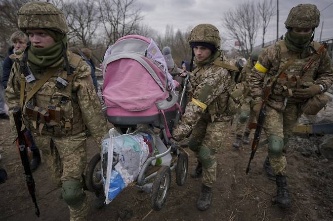 우크라이나 군인이 3월 5일 러시아의 폭격으로 무너진 다리 밑의 임시 통로에서 이르핀강을 건너려는 유아차를 나르고 있다.  AP연합뉴스