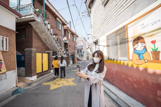 지난 8일 서울 강동구 천호대로 강풀만화거리에서 한 방문객이 유명 만화가 강풀의 웹툰 속 한 장면을 배경으로 기념사진을 찍고 있다.  강동구청 제공