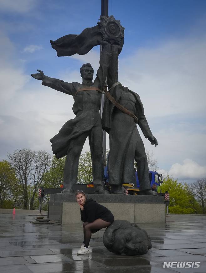 [키이우=AP/뉴시스] 26일(현지시간) 우크라이나 키이우에서 한 여성이 철거 중인 구소련 시대의 우호 상징 동상에 앉아 기념 촬영을 하고 있다. 이 동상은 우크라이나와 러시아 노동자가 '소비에트 우호 훈장'을 함께 들고 서 있는 모습으로 1982년 소련 결성 60주년 기념 공간에 설치된 것이다. 2022.04.27.