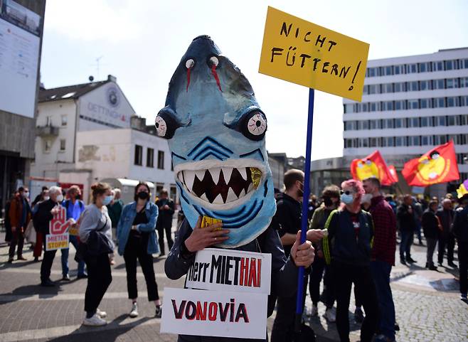 지난달 23일 독일 보훔에서 열린 월세 인상 반대 집회에서 한 참가자가 상어 의상을 입고 '상어같은 임대업자에게 먹이를 주지 맙시다'라는 팻말을 들었다. /로이터 연합뉴스