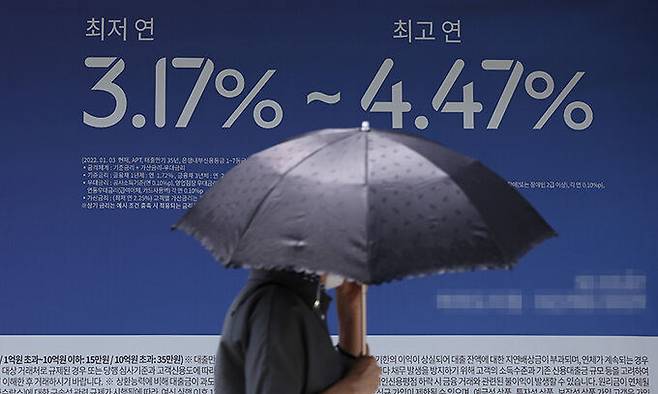 지난 25일 서울의 한 은행에 설치된 대출 관련 안내 현수막 앞으로 시민이 지나고 있다. 연합뉴스