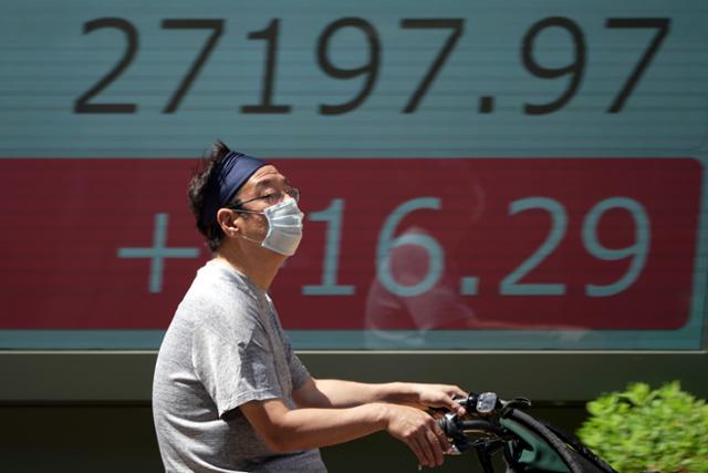 30일 도쿄에서 마스크를 쓴 남성이 자전거를 타고 증권 시세를 나타낸 전광판 앞을 지나가고 있다. 도쿄=AP 연합뉴스
