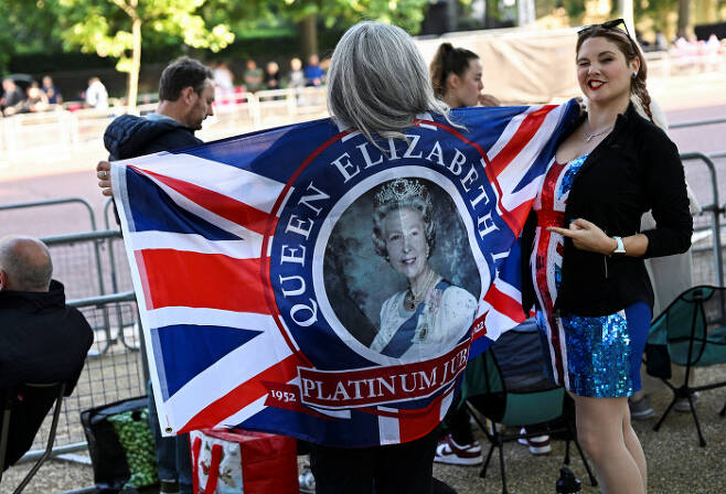 엘리자베스 2세 영국 여왕의 즉위 70주년 행사(플래티넘 주빌리) 첫날인 2일(현지시간) 런던 거리에서 한 여성이 여왕의 얼굴이 중앙에 새겨진 국기를 들어보이고 있다. 런던 | 로이터연합뉴스