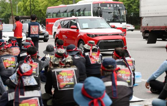 전국민주노동조합총연맹 공공운수노조 화물연대본부(화물연대) 총파업 나흘째인 10일 오후 광주 서구 기아차 생산 공장 앞에서 카캐리어를 동원하지 못해 개별 운송하는 번호판 없는 완성차량이 화물연대 노조원들의 결의대회 장소를 지나가고 있다.(이미지 출처=연합뉴스)