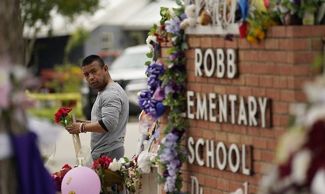 총기 난사 사건이 발생한 미국 텍사스주 유밸디 롭초등학교 앞에서 지난 5월 31일(현지시간) 시민이 추모의 꽃을 들고 있다. 18세 범인은 범행에 앞서 사회관계망서비스(SNS)에 총을 쏘겠다고 사전 고지했다. 유밸디=AP연합뉴스