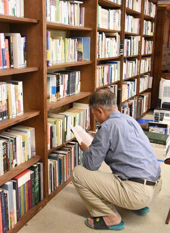 문재인 전 대통령이 맨발 차림으로 서재 앞에 쪼그려 앉아 책을 살피고 있는 모습.