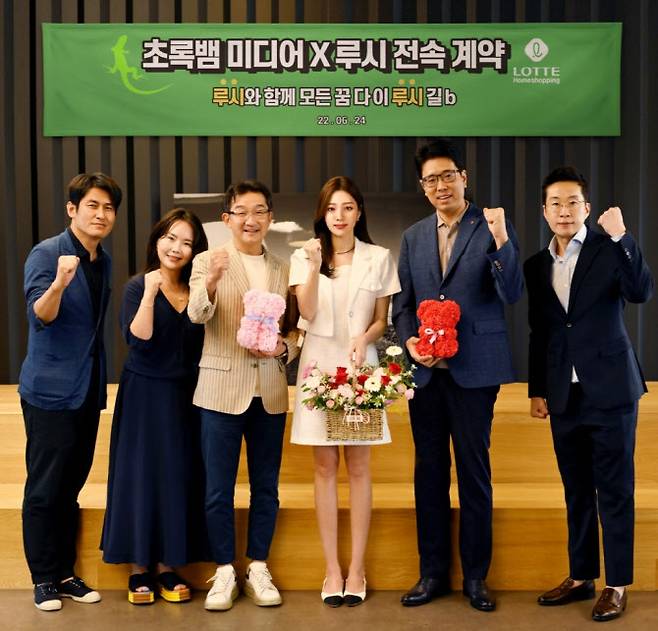 롯데홈쇼핑이 개발한 가상인간 ‘루시’(오른쪽 세번째)가 지난 24일 서울 서초구 초록뱀미디어 본사에서 초록뱀미디어와 아티스트로 전속 계약을 체결하고 기념 촬영을 하고 있다.(사진=롯데홈쇼핑)